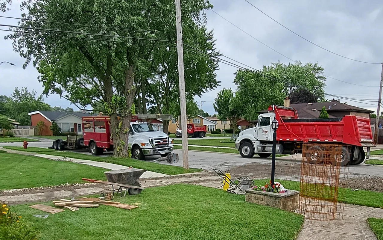 Dump trucks lined up along the street for a driveway replacement